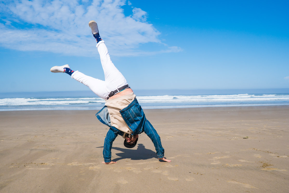 A male model performs a cartwheel on the beach shore.