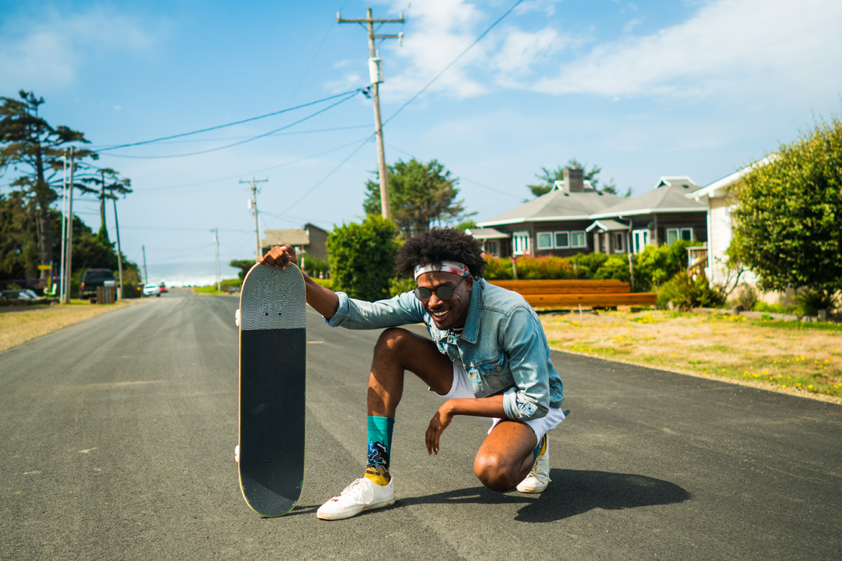 A male model rides a skateboard down a road.