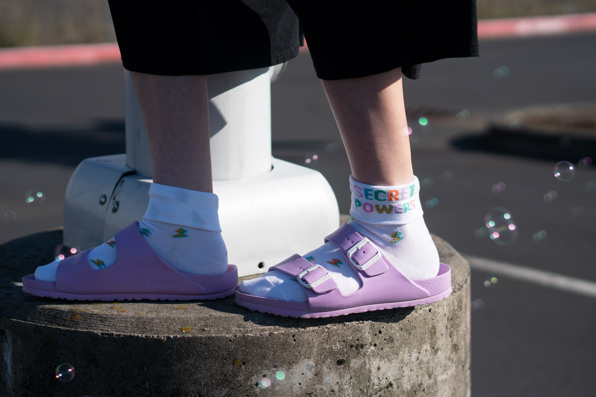 An adult's and toddler's legs wearing matching purple panda socks. They are standing on a sidewalk.