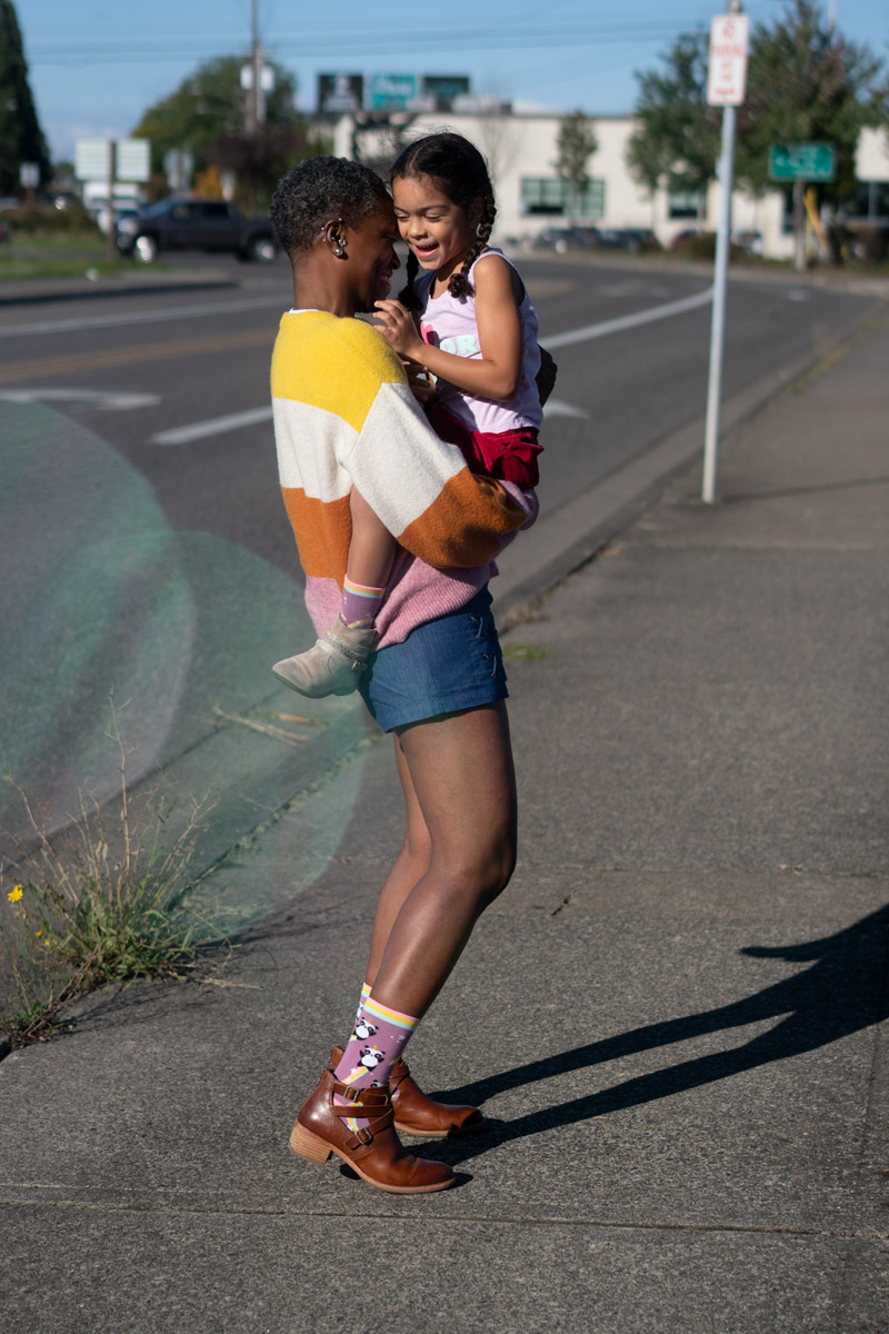 A mom holding her child on a sidewalk. The child is smiling at the camera while bubbles surround her.