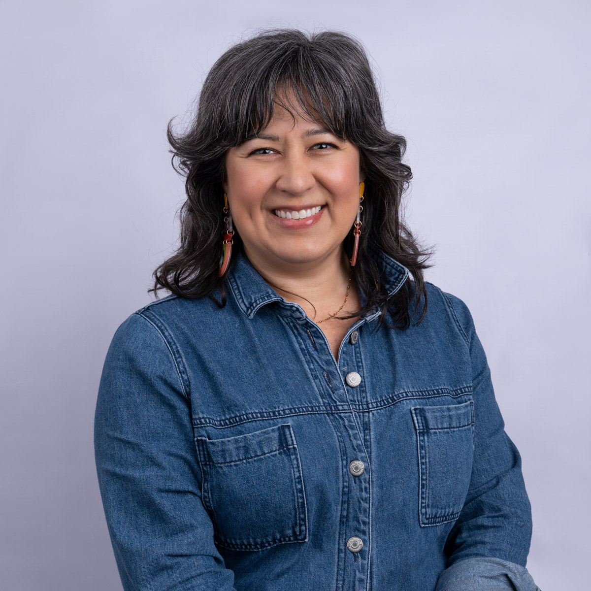 A woman wearing a denim jacket, smiling in front of a white backdrop.