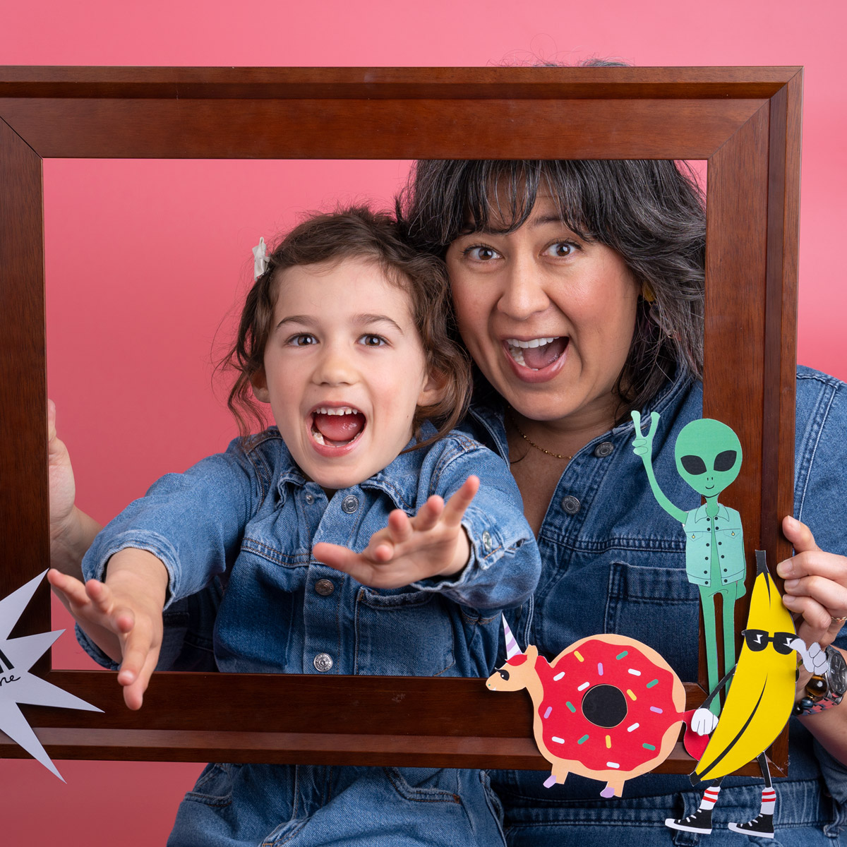 A child and her mom yelling while holding an empty wooden frame in front of them.
