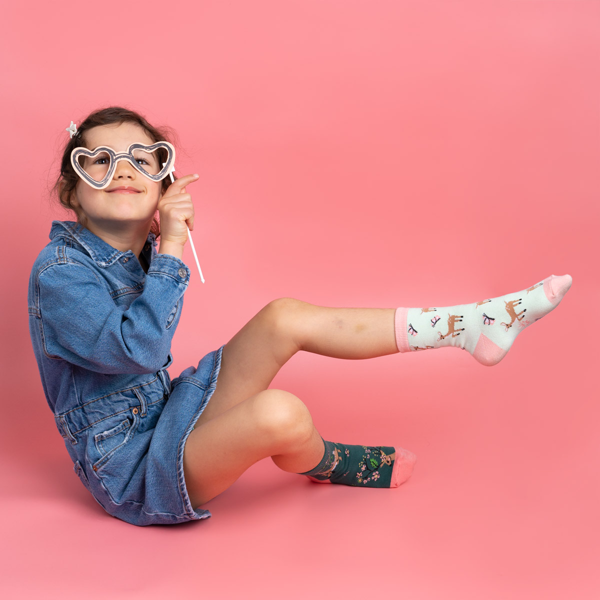 A child sitting on a pink backdrop, while holding out one foot in the air.
