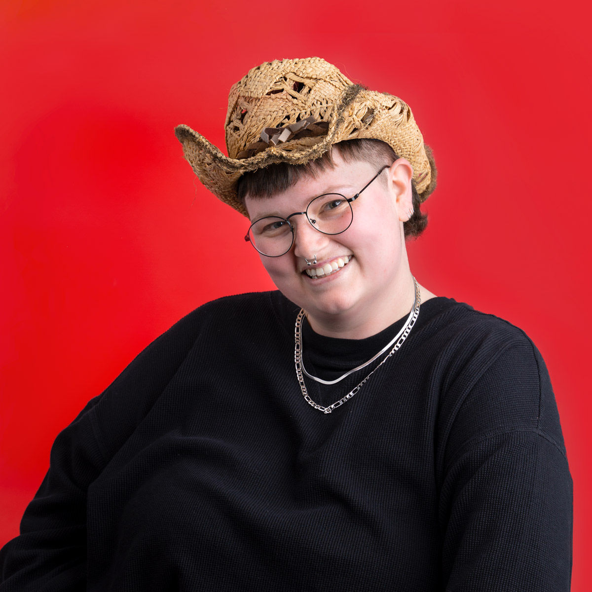 A person wearing a 10 gallon hat while smiling in front of a red backdrop.