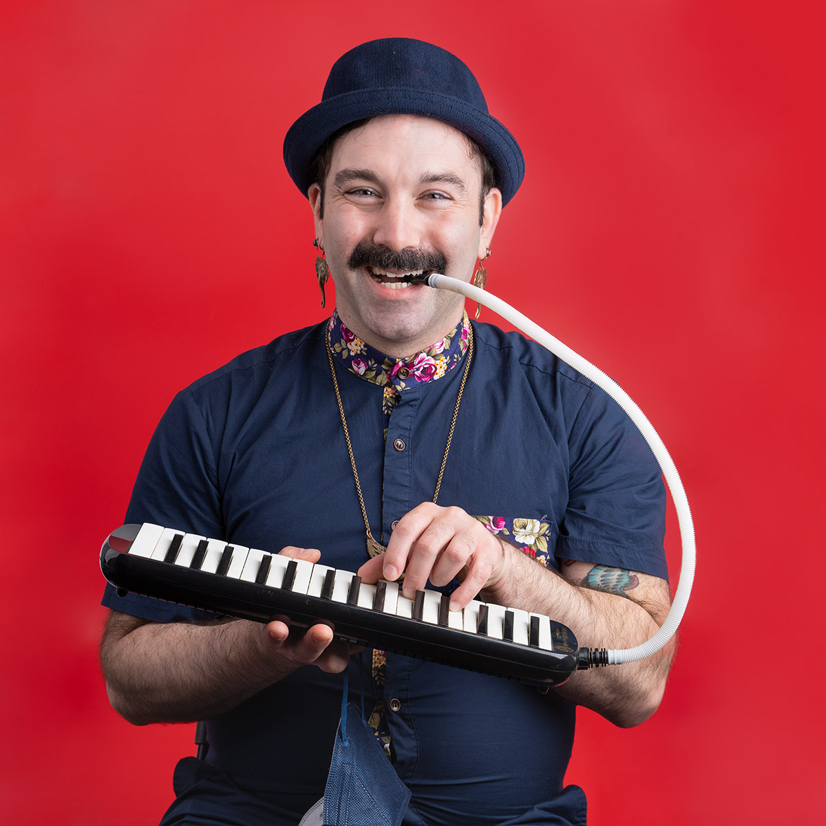 A person smiling an playing a mouth piano. Sitting in front of a red backdrop.